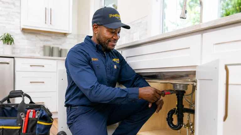 Positive Plumbing technician repairing pipes beneath a kitchen sink in Orange County